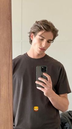 a young man looking at his cell phone while standing in front of a mirror with the door open