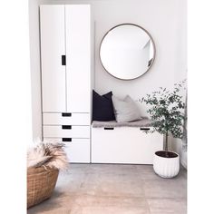 a room with white furniture and a round mirror on the wall, along with a potted plant