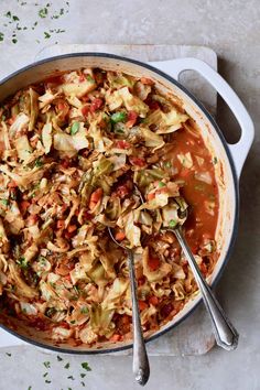 a large pot filled with cabbage and other vegetables next to two spoons on a table