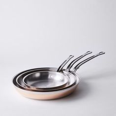 three stainless steel pans with spoons in them sitting side by side on a white surface