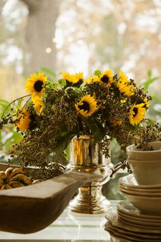 sunflowers and other flowers in a silver vase on a window sill next to dishes