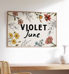 a white vase sitting on top of a wooden table next to a sign that says violet june