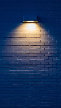 a blue brick wall with a lamp on it's side in the night time