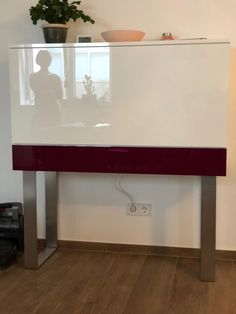 a white and red cabinet sitting on top of a hard wood floor next to a plant