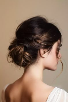 a woman with her hair in a low bun, wearing a white top and looking off to the side