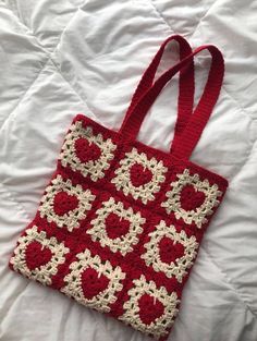 a red and white crocheted bag laying on top of a bed next to a pillow