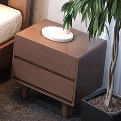 a potted plant sitting on top of a wooden table next to a bed and nightstand