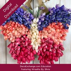 a heart shaped wreath with purple and pink flowers hanging from the front, on a white wooden background