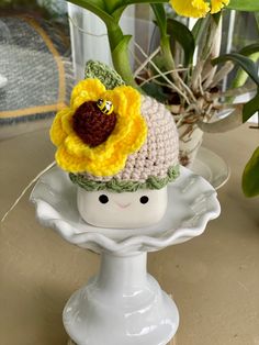 a crocheted hat with a yellow flower on top sits on a white plate