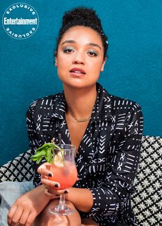 a woman sitting on a couch holding a drink in her hand and looking at the camera