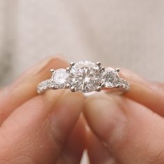 three stone diamond ring being held by someone's hand