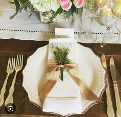 a place setting with napkins, silverware and flowers in the centerpiece on a wooden table