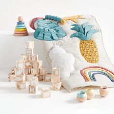 an assortment of wooden toys on a white surface next to a pillow with a pineapple design