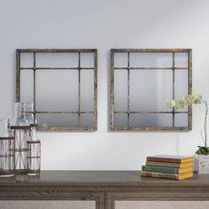 two mirrors are hanging on the wall above a table with books, vases and flowers