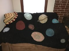 a black blanket with multicolored crocheted circles on it next to a window