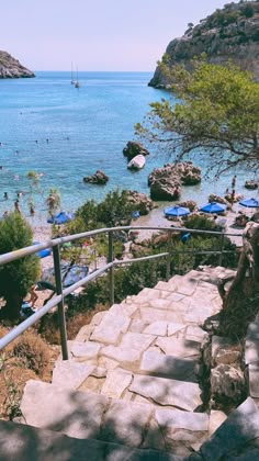 stairs lead down to the beach with blue umbrellas on them and people swimming in the water