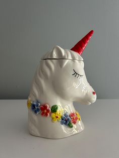 a white ceramic unicorn with a red horn and flowers around it's head on a table