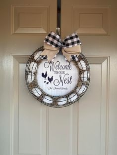 a welcome to our nest wreath hanging on the front door with a bow around it