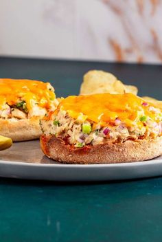 an open faced sandwich with chicken and cheese on it sitting on a plate next to a pickle