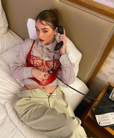 a woman sitting on a bed while talking on the phone and holding a telephone to her ear