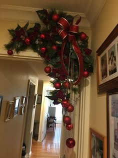 a christmas wreath hanging from the ceiling with red ornaments and bows on it's side