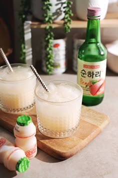 two glasses filled with liquid sitting on top of a wooden cutting board next to bottles