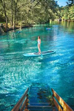 a woman standing on a surfboard in the middle of a river with blue water