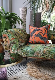 a green couch with an orange and black pillow on it next to potted plants