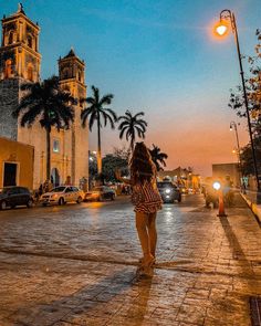 a woman walking down the street in front of an old church at dusk with palm trees