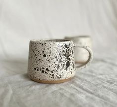 two white and black mugs sitting on top of a bed