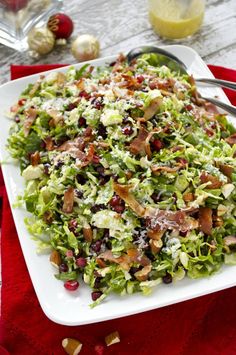 a salad with bacon and cranberries on a white plate next to silverware