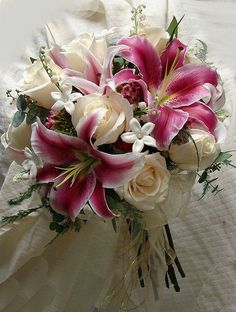 a bridal bouquet with white roses and pink lilies on a bed in the sunlight