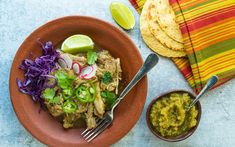 a plate of food with tortillas, salsa and limes on the side