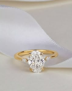 an oval cut diamond engagement ring on a white satin ribbon with the center stone set in yellow gold