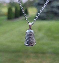 a silver bell hanging from a chain in front of a green field with trees and grass