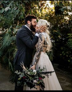 a man in a suit and tie kissing a woman with tattoos on her arms, wearing a wedding dress