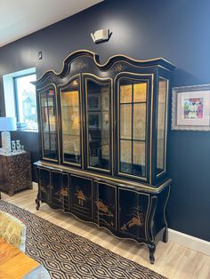 a black and gold china cabinet with glass doors on the front, in a living room