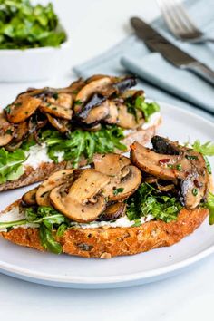 two slices of bread with mushrooms on top and lettuce in the middle, sitting on a white plate