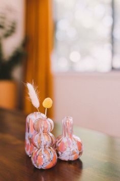 two small vases sitting on top of a wooden table next to each other with a feather sticking out of them