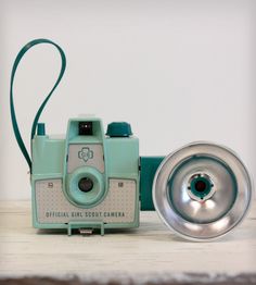 an old camera sitting on top of a wooden table next to a metal bowl and speaker