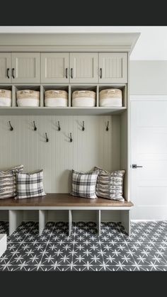 a bench with pillows on it in front of some white cupboards and shelves filled with baskets