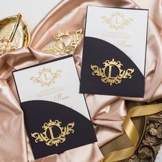 two black and gold wedding cards with the letter d on them next to a golden ribbon