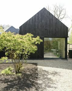 a black house with a tree in the front yard and gravel area on the side