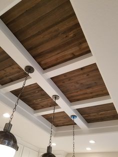 two lights hanging from the ceiling in a kitchen with wood paneling and white cabinets