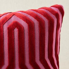 a red and pink striped pillow sitting on top of a wooden table next to a white wall