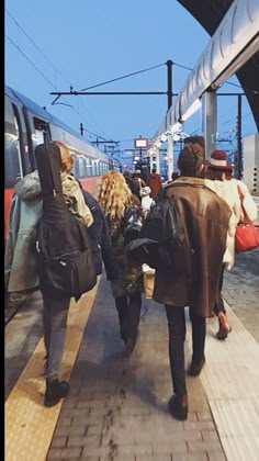 several people walking on the platform next to a train