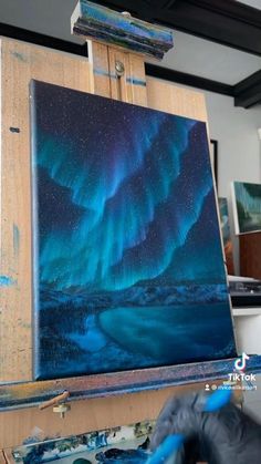 an easel with some paintings on it and the aurora bore in the sky above