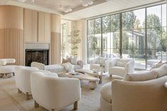 a living room filled with lots of white furniture next to a fire place and large windows