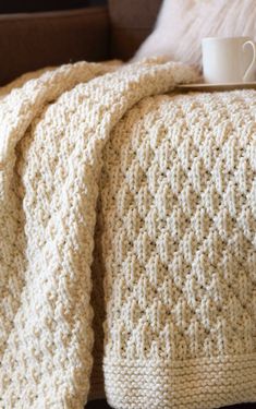 a coffee cup is sitting on top of a crocheted blanket that has been folded over