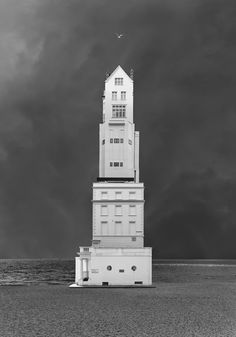 a black and white photo of a tall building on the water with an airplane flying over it